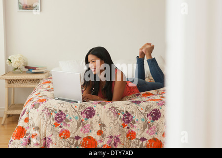 Chinese woman using laptop on bed Stock Photo