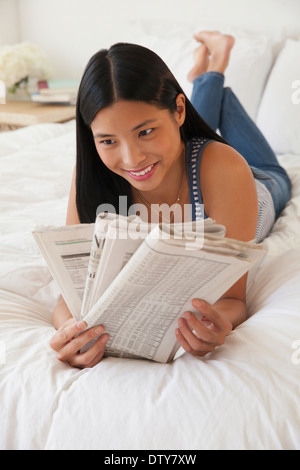 Chinese woman reading newspaper on bed Stock Photo