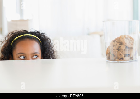 Mixed race girl peering at cookie jar Stock Photo