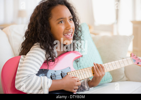 Mixed race girl playing electric guitar on sofa Stock Photo