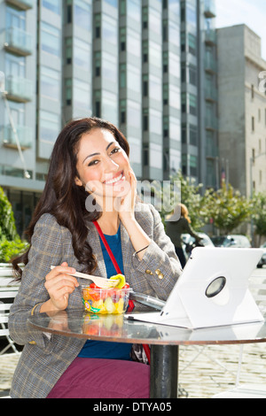 Mixed race woman eating lunch at urban sidewalk cafe Stock Photo