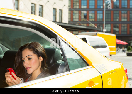 Mixed race woman using cell phone in taxi Stock Photo