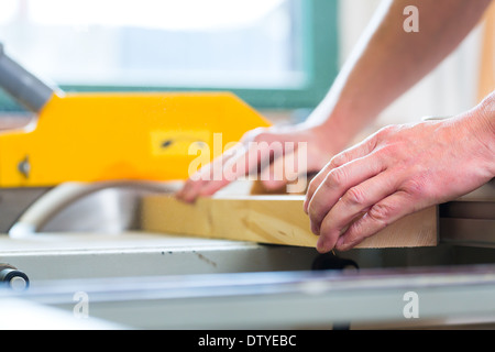Carpenter working on an electric buzz saw and cutting some boards in carpentry Stock Photo