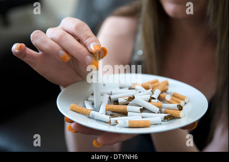 cigarette stub synonym A woman stubs a cigarette stub out in an ashtray of other cigarettes in an  attempt to quit smoking Stock Photo