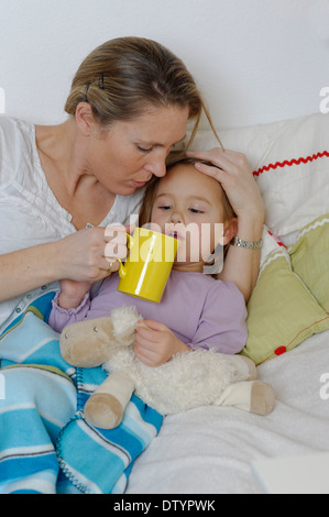Mother taking care of her sick daughter, dispensing hot tea, girl lying in bed