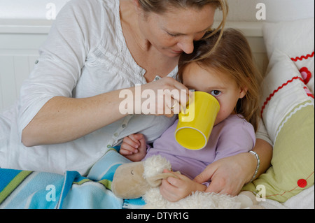 Mother taking care of her sick daughter, dispensing hot tea, girl lying in bed