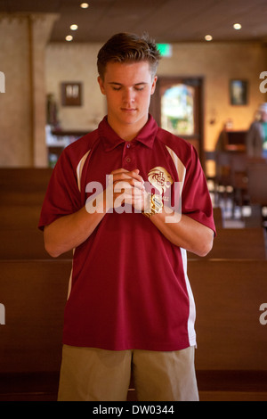 A uniformed student at a private Catholic high school in San Juan Capistrano, CA, prays in the school's chapel. Stock Photo