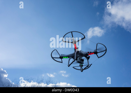 Miniature drone / unmanned aerial vehicle / UAV equipped with camera in flight against blue sky with clouds Stock Photo