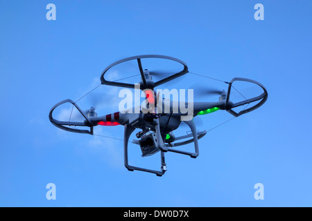 Miniature drone / unmanned aerial vehicle / UAV equipped with camera in flight against blue sky with clouds Stock Photo