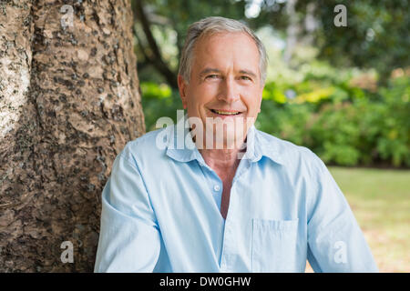 Happy retired man sitting on tree trunk Stock Photo