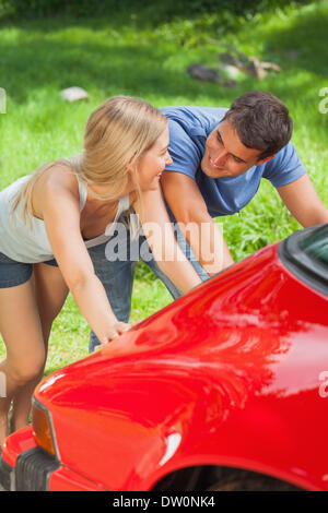 Happy couple pushing their broken down car Stock Photo