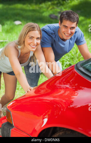 Smiling couple pushing their broken down car Stock Photo