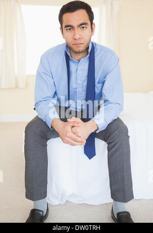 Unsmiling man sitting on his bed Stock Photo