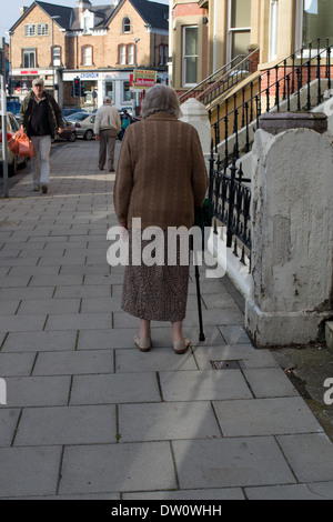 Rear view of old lady walking aided with a stick Stock Photo