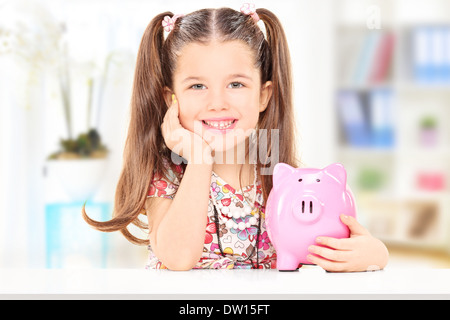 Cute girl sitting at table and holding her savings at home Stock Photo