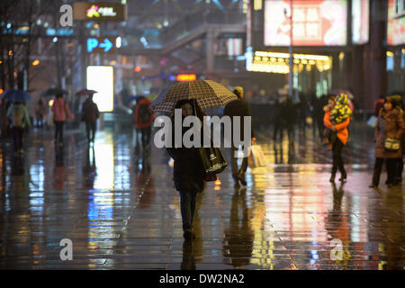 Beijing, China. 26th Feb, 2014. A pedestrian walks in the rain in Xidan, a commercial area in Beijing, capital of China, Feb. 26, 2014. Beijing saw its first rain this spring on Wednesday evening. The precipitation would be conducive to the city's air quality, which had been marred by a lingering smog. © Li Xin/Xinhua/Alamy Live News Stock Photo