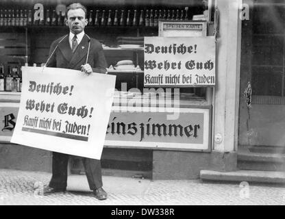 A man, who wears a poster around his neck reading 'Germans! Defend yourselves! Do not by from Jews!', stands in front of a Jewish shop, around 1933. This slogan subsumed a rich boycott of Jewish shops, doctors and lawyers, which began on 01 April 1933. The anti-Semitic campaign was organized by the 'Central Committee for the Defence of the Jewish atrocity and boycott agitation'. Fotoarchiv für Zeitgeschichtee / NO WIRE SERVICE Stock Photo