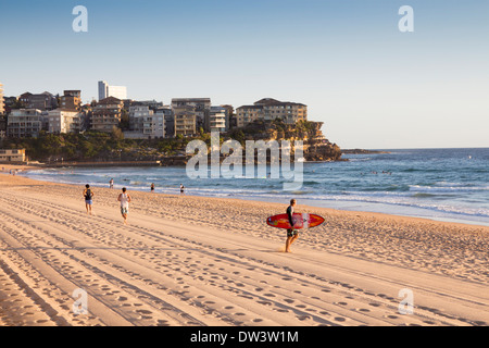 Manly North Steyne beach Surfer walking towards sea, runners in background Northern Beaches Sydney New South Wales NSW Australia Stock Photo
