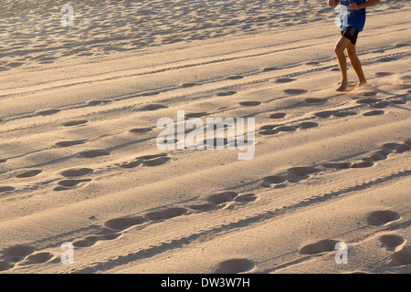 Footprints and tyre tracks in sand at dawn with runner in top corner of frame North Steyne Beach Manly Sydney NSW Australia Stock Photo