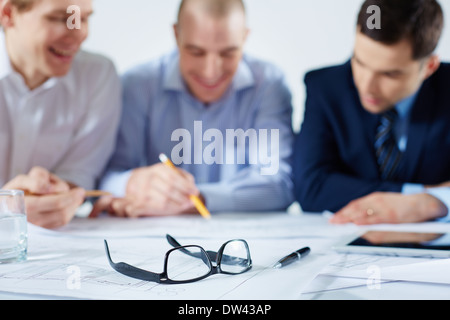 Closeup image of eyeglasses and a ballpoint on the table where business colleagues sharing the ideas on the foreground Stock Photo