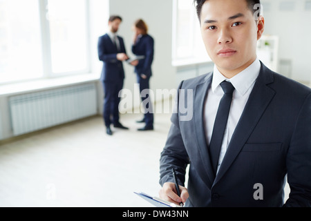 Young businessman writing plan and looking at camera in working environment Stock Photo