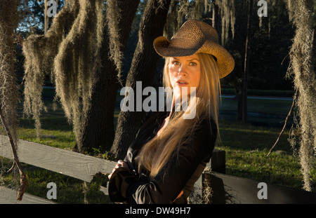 attractive 50 year old blonde woman cowgirl with a hat outdoors leaning against fence with spanish moss Stock Photo