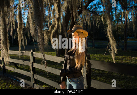 attractive 50 year old blonde woman cowgirl with a hat outdoors leaning against fence with spanish moss Stock Photo