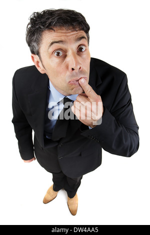 Startled business looking up at the camera in wide eyed amazement with his finger raised to his lips, high angle fun portrait is Stock Photo