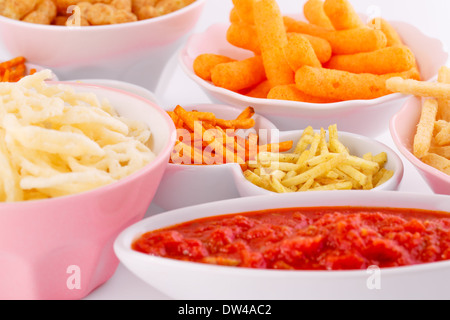 Potato, corn and wheat chips in bowls and red sauce isolated on gray background. Stock Photo
