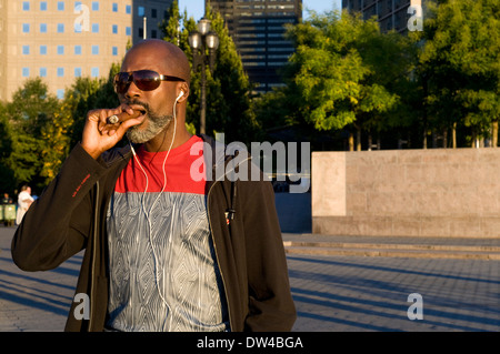 An American smokes a cigar in Battery Park. This park is in the south-west side of downtown Manhattan, adjacent to the Financial District and Ground Zero. In Battery Park City's many restaurants, it's worth taking a 'brunch' watching the river and the buildings of New Jersey, and a great walk along the Hudson. In this park we can see the Castle Clinton or catch ferries leading to Liberty Island (where the famous Statue of Liberty) and Ellis Island. Stock Photo