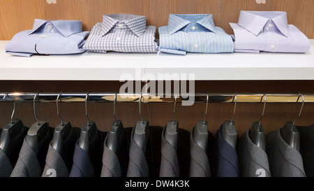 Row of men suit jackets on hangers and shelf with shirt in clothing store Stock Photo