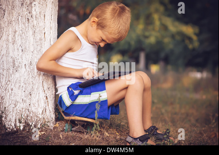 Boy Child playing with Tablet PC Outdoor with Summer nature on background Computer Game Dependence concept Lifestyle Stock Photo