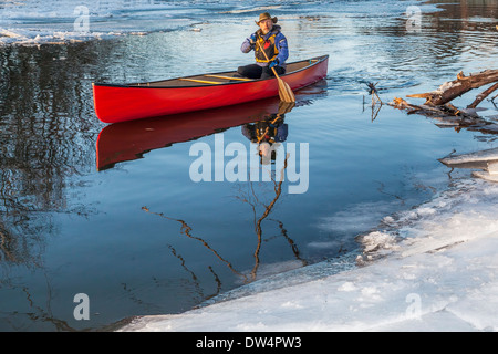 a senior male paddling a red canoe in winter - Cache la Poudre River in Fort Collins, Colorado Stock Photo