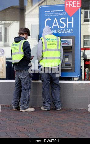 Two young men in Builders Work Clothes withdraw cash from a Nationwide Building Society ATM or Cash Machine Stock Photo