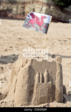 A sand castle on a sandy beach topped with the Welsh national flag Stock Photo