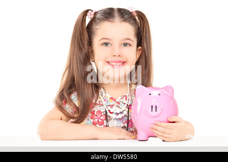 Little girl sitting at table and holding a piggybank Stock Photo