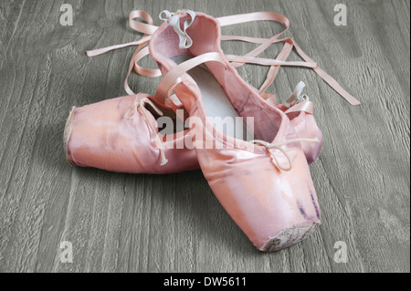 Old used pink ballet shoes on wooden background Stock Photo