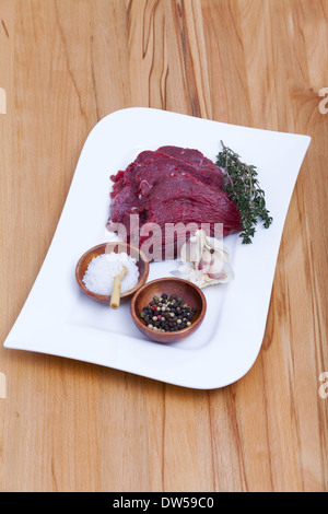 Four Slice Beef Tenderloin with a twig Thyme, Peppercorns, Garlic and Salt on a Plate on wooden Kitchen Worktop Stock Photo