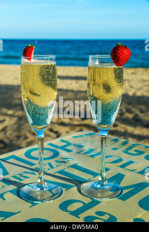 Two glasses of sparkling wine on the table with sandy beach and sea in the background Stock Photo