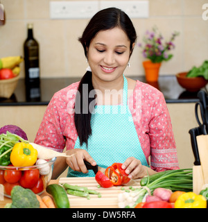 Smiling young Indian woman cutting vegetables Stock Photo