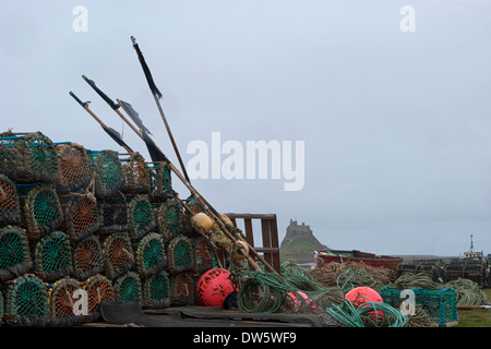 The distinctive silhouette of Lindisfarne castle visible behind Lobster pots and diverse lobster fishing equipment Stock Photo