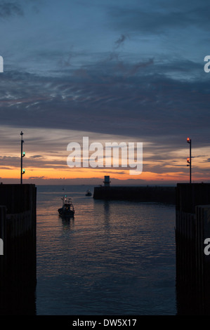 A boat presenting itself to the harbour lock gates at dusk in Whitehaven Harbour. Beautiful colours in the sky. Stock Photo