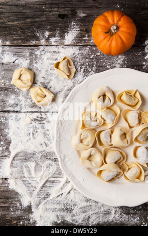 Top view on plate of homemade pasta ravioli over wooden table with flour and orange pumpkin Stock Photo