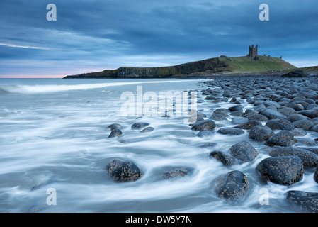 The ruins of Dunstanburgh Castle overlooking the boulder strewn shores of Embleton Bay, Northumberland, England. Stock Photo