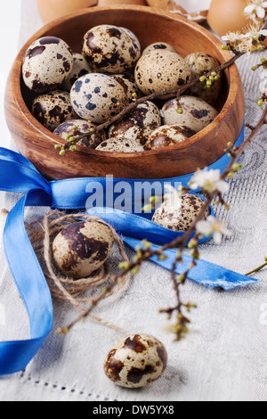 Wooden bowl of quail eggs with blossom branch and blue tape over gray textile napkin Stock Photo