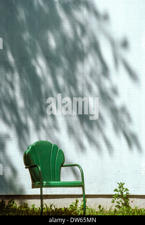 vintage metal seashell lawn chair in front of sunlit wall and shadows of branches Stock Photo