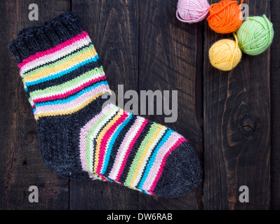 Pair of colorful striped woolen socks on dark wooden vintage background with multicolored balls of yarn and room for copy space Stock Photo