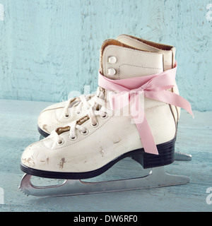 Pair of white women's ice skates on blue vintage wooden background with pink ribbon Stock Photo