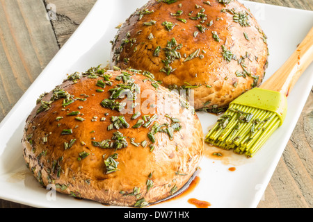 Two portobello mushrooms brushed and marinating in balsamic vinegar, olive oil and rosemary Stock Photo