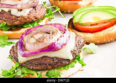 Portobello burgers on a bed of arugula, topped with melted swiss cheese, grilled purple onion, avocado and tomato Stock Photo